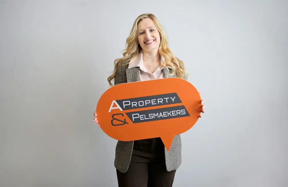 Smiling woman holding a "property & pelsmakers" sign, illustrating property valuation and appraisal